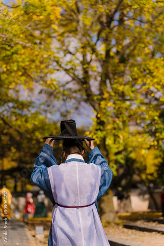 a person in traditional Korean attire, standing under a canopy of vibrant yellow autumn leaves in Jeonju, creating a serene and culturally rich scene