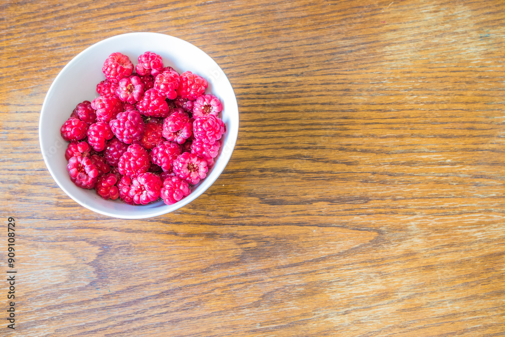 A selection of vibrant fresh raspberries arranged in a white bowl placed on a wooden table A selection of vibrant fresh raspberries arranged in a white bowl placed on a wooden table