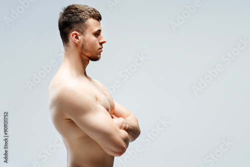 Canvastavla Fit man standing sideways crossing arms showing muscles, looking away isolated o