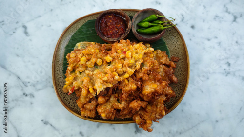 Golden Brown Bakwan Jagung or Indonesian Corn Fritters with Chili Sauce and Fresh Green Chili on Rustic Plate on Marble Table photo