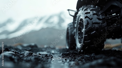 Close-up of a rugged, mud-splattered off-road vehicle's tire on rocky, mountainous terrain, depicting adventure and endurance against a backdrop of snowy peaks. photo