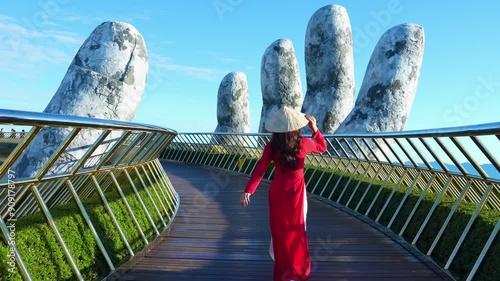 4k slow motion,Asian woman wearing red.Vietnamese culture with traditional conical hat withon the Golden han Bridge, Da Nang City, Vietnam. photo