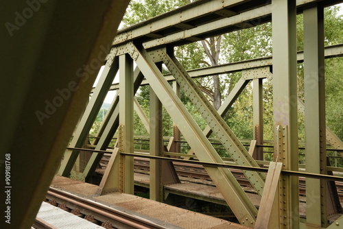 An old railroad bridge with a steel structure and trees in the background.