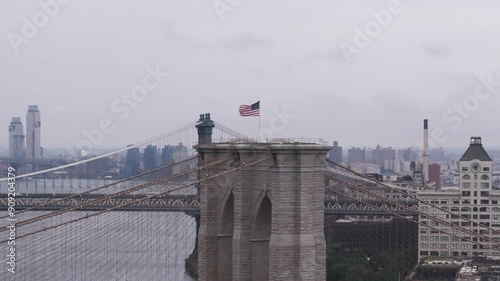 Aerial orbit shot around American flag standing on top of the Brooklyn bridge