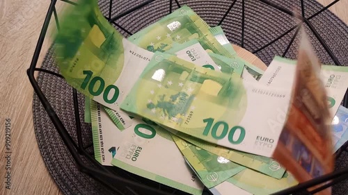 View of 100 euro and other euro banknotes falling into a dark basket