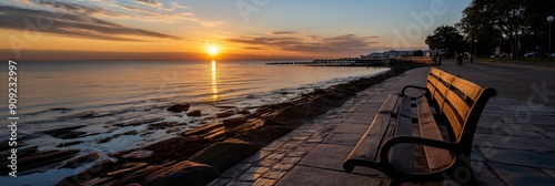 Solitude by the Sea: A solitary bench sits on a stone path overlooking a tranquil sea, bathed in the golden hues of a breathtaking sunrise. The scene evokes a sense of peace, reflection, and the promi photo