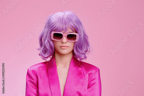 Purplehaired woman in sunglasses and a pink suit stands confidently against a matching pink background, showcasing a bold and vibrant fashion choice photo