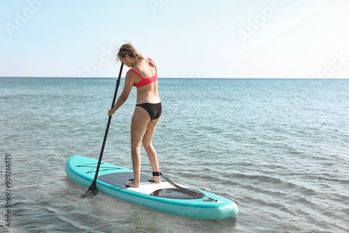 Beautiful teen girl floating on a blue sup board, practicing paddle. The concept of water sports, relaxation, summer holidays, self-immersion. Teenager alone on board against background of water, sea.