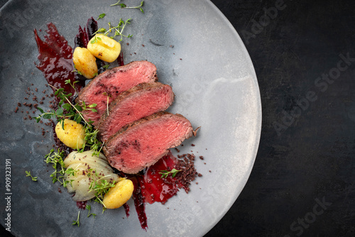 Traditional fried venison back filet with sliced pear, gnocchi and plum jam served as close-up on Nordic design plate with copy space right