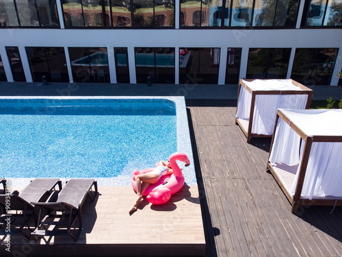 Aerial drone view of woman relaxing on flamingo pool float in pool in hotel. Summer holidays, enjoying summer vacations, luxury hotel