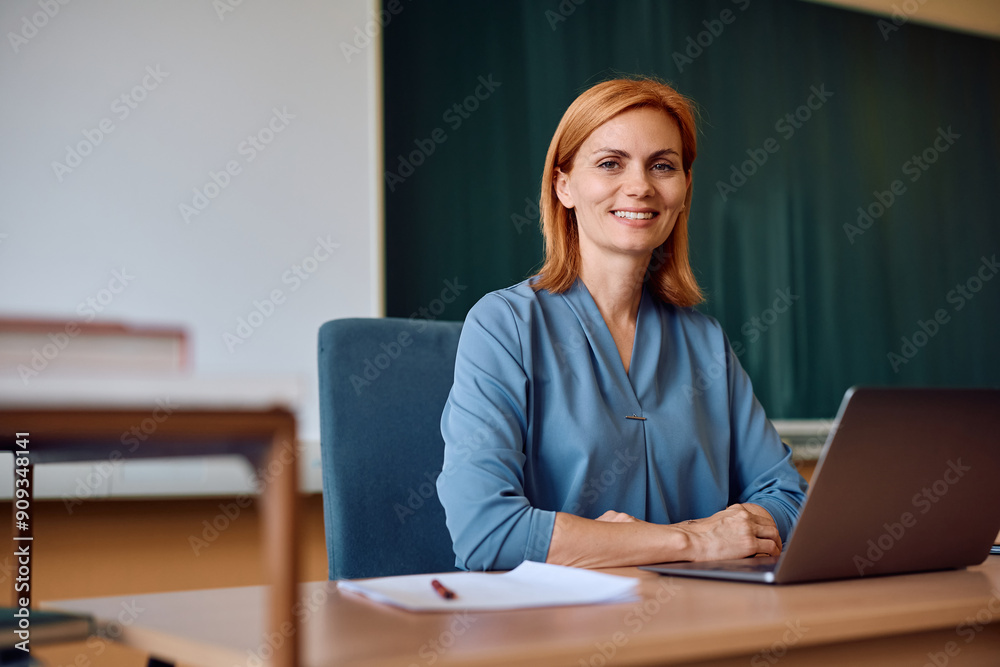Happy female teacher using laptop in classroom and looking at camera. Happy female teacher using laptop in classroom and looking at camera.