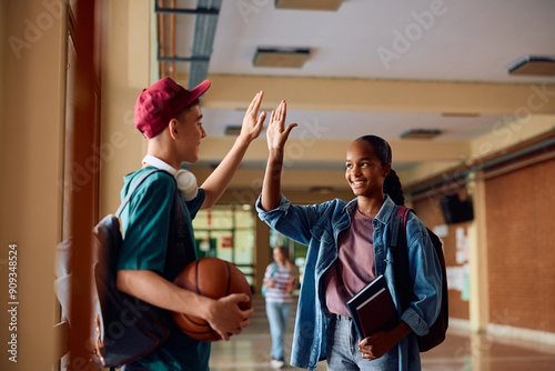 Happy high school friends giving high-five in hallway.