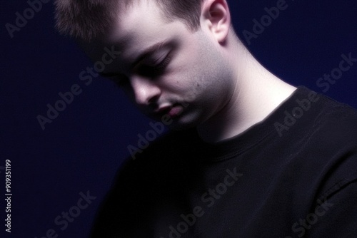 Thoughtful Young Man in Dark Shirt Against Dim Blue Background Contemplating with Closed Eyes