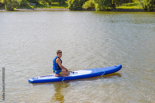 A young guy sitting down rides a SUP board, overcoming the waves with ease