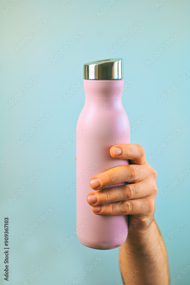 Closeup hand holding pink metal water bottle mock up isolated on blue background, water container, template, copy space area