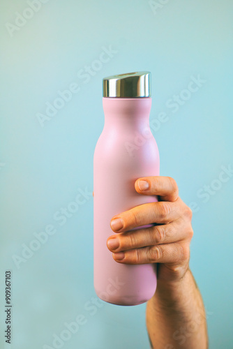 Obraz na płótnie Closeup hand holding pink metal water bottle mock up isolated on blue background, water container, template, copy space area w salonie