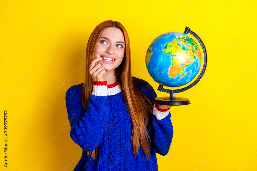 Photo portrait of pretty young girl hold globe look empty space wear trendy blue knitwear outfit isolated on yellow color background Photo portrait of pretty young girl hold globe look empty space wear trendy blue knitwear outfit isolated on yellow color background
