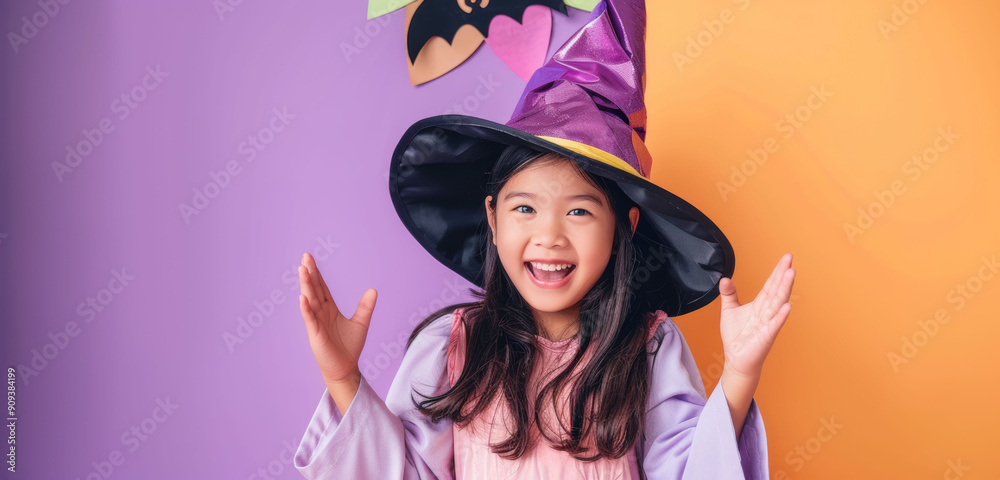 A young joyful girl in a witch costume is excitedly posing with an orange and purple background, representing Halloween festivities. A young joyful girl in a witch costume is excitedly posing with an orange and purple background, representing Halloween festivities.