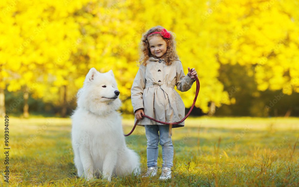 Φωτογραφία Happy child girl with white Samoyed dog walking together in sunny autumn park
