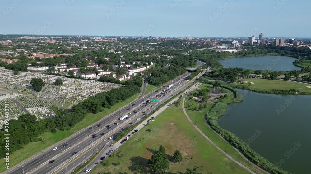 cars driving on an urban road with skyline view (queens new york city) busy highway traffic (cars, trucks) cemetery and lake with residential buildings in background (corona flushing meadows park)