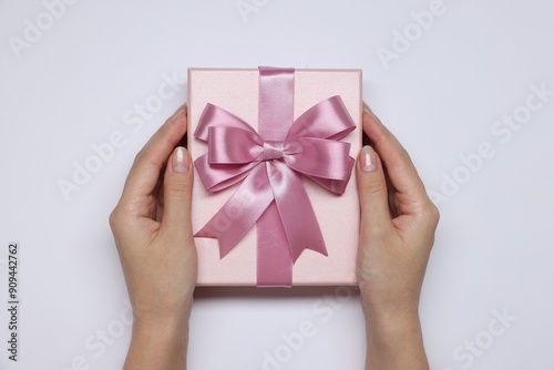 Fototapeta Naklejka Na Ścianę i Meble -  Woman holding gift box with bow on white background, top view