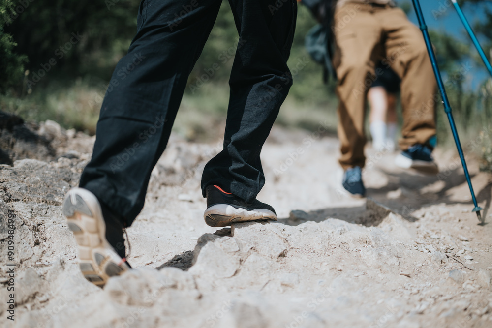 Close-up image of two hikers walking on a rocky trail in the mountains, focusing on their shoes and legs. Close-up image of two hikers walking on a rocky trail in the mountains, focusing on their shoes and legs.