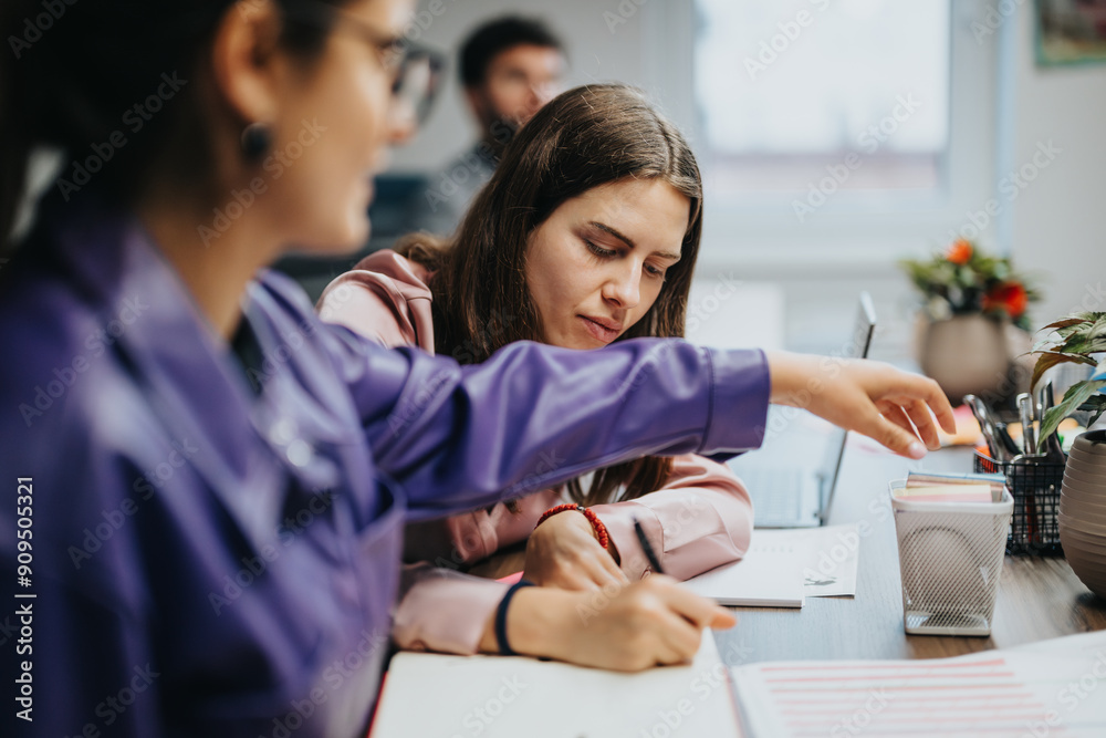 Φωτογραφία Two female colleagues engaged in a business meeting at a desk, focusing on documents and discussing details intensely in an indoor office setting