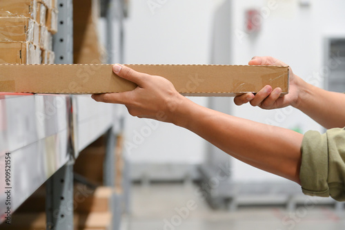 Billede på lærred Hands holding a long cardboard box, focusing on proper storage in a warehouse environment