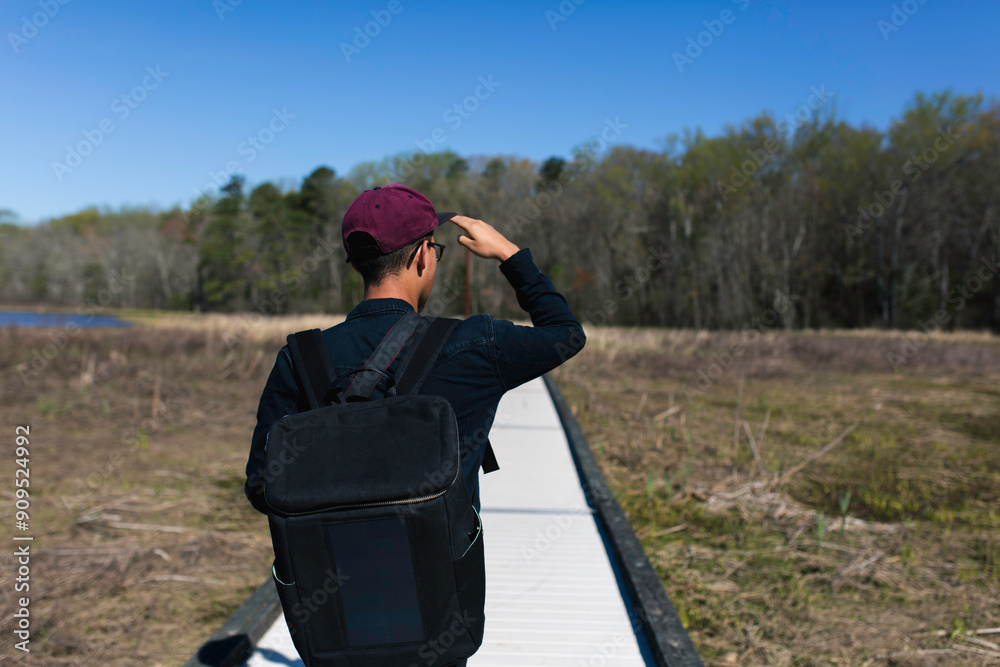 Person With A Solar Backpack Walking Along A Wooden Path In A Natural Setting Person With A Solar Backpack Walking Along A Wooden Path In A Natural Setting