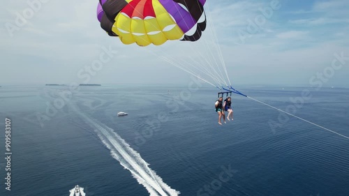 Couple on Summer Vacation Parasailing From Boat Over Blue Sea, Drone Dolly in Towards People, then Follow Locked in photo