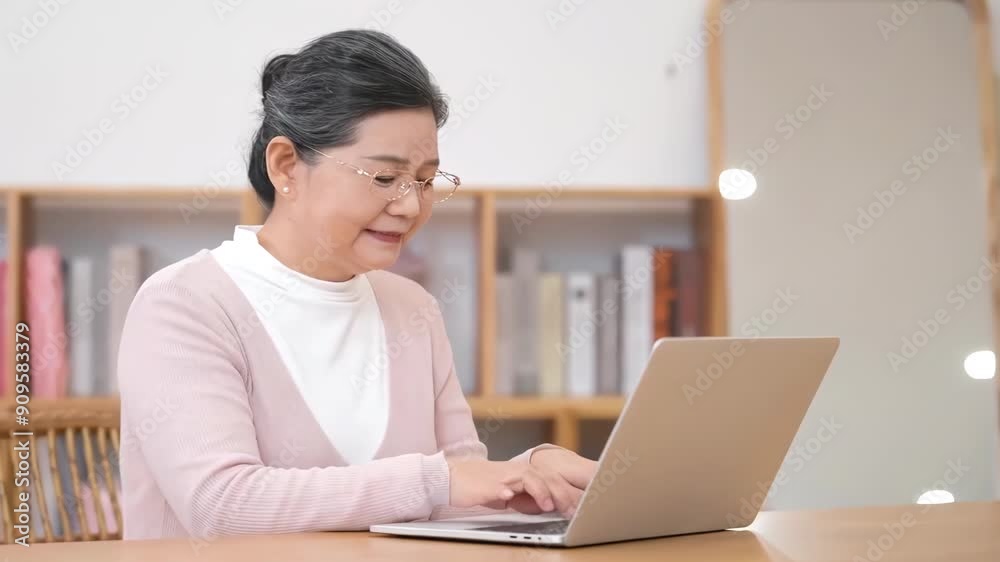 Senior elderly woman with glasses uses laptop to type on sofa in cozy living room to communicate and entertain in their home life. Adult female enjoying technology and communication. Senior elderly woman with glasses uses laptop to type on sofa in cozy living room to communicate and entertain in their home life. Adult female enjoying technology and communication.