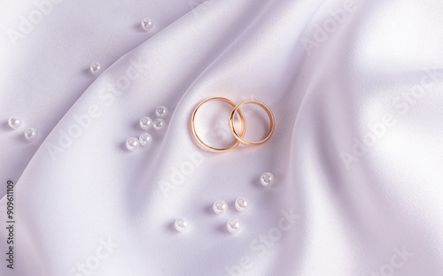 Chic wedding background with wedding gold rings lying on a wave of white satin fabric and pearls. The concept of the wedding. postcard. top view. photo