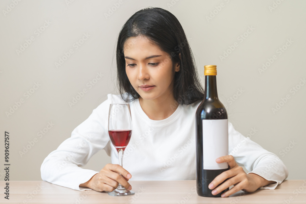 Alcoholism drunk asian young woman hand holding glass of red wine with whiskey bottle, female sitting alone, drinking on table at home. Treatment of alcohol addiction, suffer abuse problem alcoholism Alcoholism drunk asian young woman hand holding glass of red wine with whiskey bottle, female sitting alone, drinking on table at home. Treatment of alcohol addiction, suffer abuse problem alcoholism