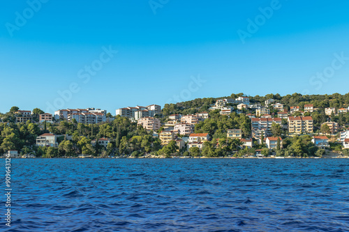 Scenic Croatian coast near Split, featuring lush green hills, charming houses, and vibrant blue skies. A serene Mediterranean landscape perfect for a tranquil getaway.