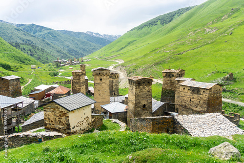 Fototapeta Naklejka Na Ścianę i Meble -  Stone towers with loopholes and small church. Green mountains and cloudy sky in the background. Fortress towers and streets of the Ushguli village.