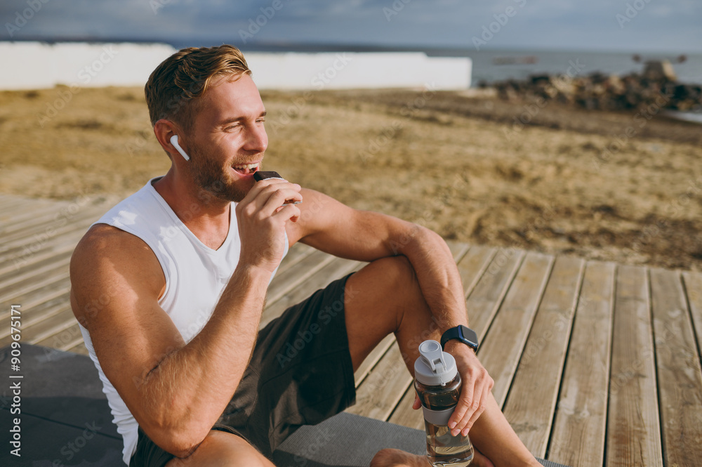 Ταπετσαρία Young strong sporty athletic toned fit sportsman man he wears sports clothes eat protein bar drink water warm up train at sunrise sun dawn over sea beach outdoor on pier seaside in summer day morning