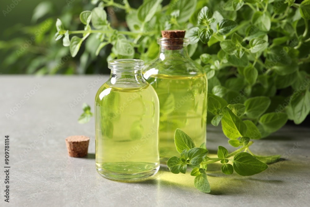 Essential oil in bottles and oregano twigs on light grey textured table, closeup Essential oil in bottles and oregano twigs on light grey textured table, closeup