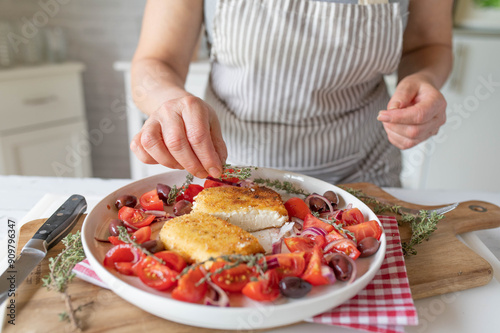 Fresh and homemade breaded feta cheese with tomato olive salad prepared by woman´s hands in the kitchen