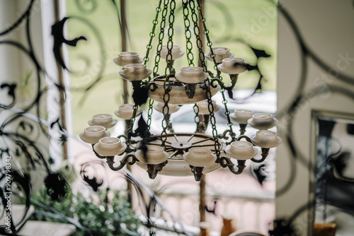 Cesis, Latvia - July 12, 2024 - An ornate chandelier with multiple candle-shaped lights hangs from the ceiling, viewed through decorative wrought iron patterns.