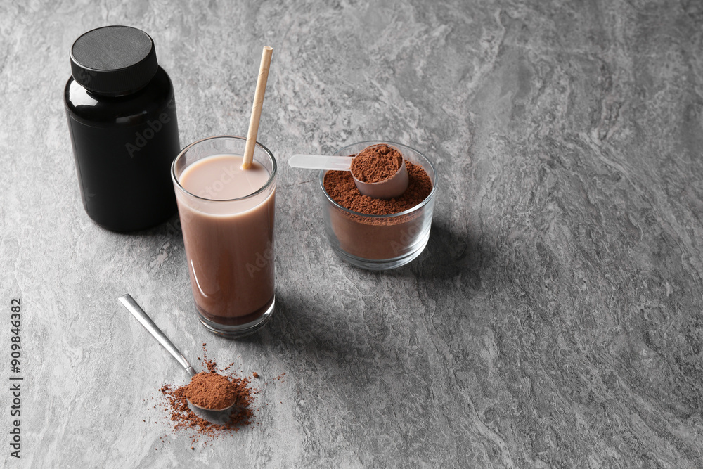 Fototapeta premium Delicious protein shake in glass, powder, spoon and plastic bottle on grey table, space for text