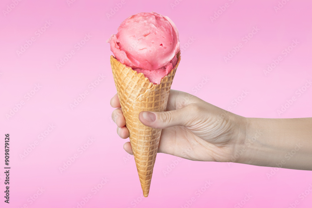 Woman's hand holding waffle cone with strawberry ice cream on pink background food Woman's hand holding waffle cone with strawberry ice cream on pink background food