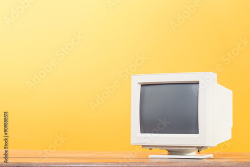 Retro desktop computer CRT monitor screen on old wooden desk front yellow background. Vintage style filtered photo