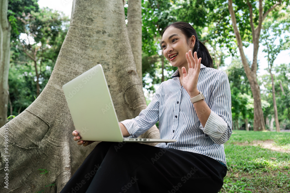 Young Professional Woman Working Remotely on Laptop in Park, Engaging in Virtual Meeting, Smiling and Waving Young Professional Woman Working Remotely on Laptop in Park, Engaging in Virtual Meeting, Smiling and Waving
