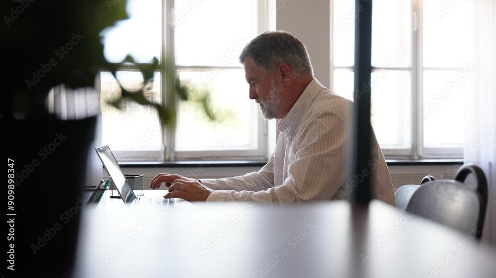 Creative mature entrepreneur typing on laptop, browsing the internet and searching customer emails. Smiling, happy and ambitious business man working on innovation and a startup vision