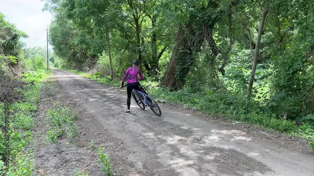 Woman cycling through a peaceful forest trail on a sunny day, surrounded by lush greenery and tall trees, enjoying nature and fresh air Woman cycling through a peaceful forest trail on a sunny day, surrounded by lush greenery and tall trees, enjoying nature and fresh air