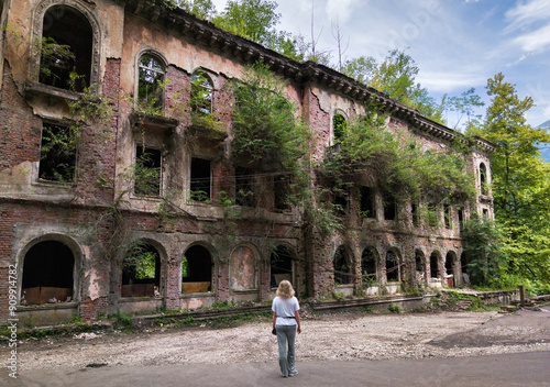 Abandoned building in Akarmara town, Tkvarcheli city, Abkhazia. Old ruins overgrown by grass and ivy in summer. Concept of war, grunge, architecture, nature photo