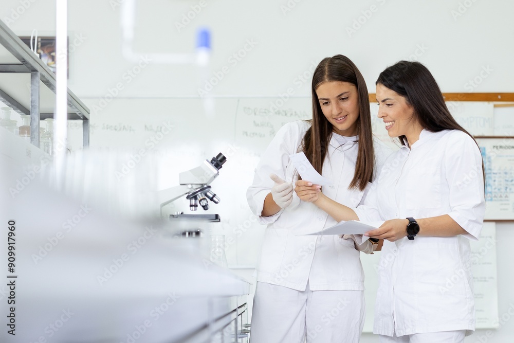 Two women in lab coats reviewing documents in lab Two women in lab coats reviewing documents in lab