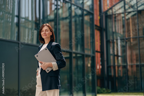 A confident businesswoman is working on a laptop outside a contemporary office building