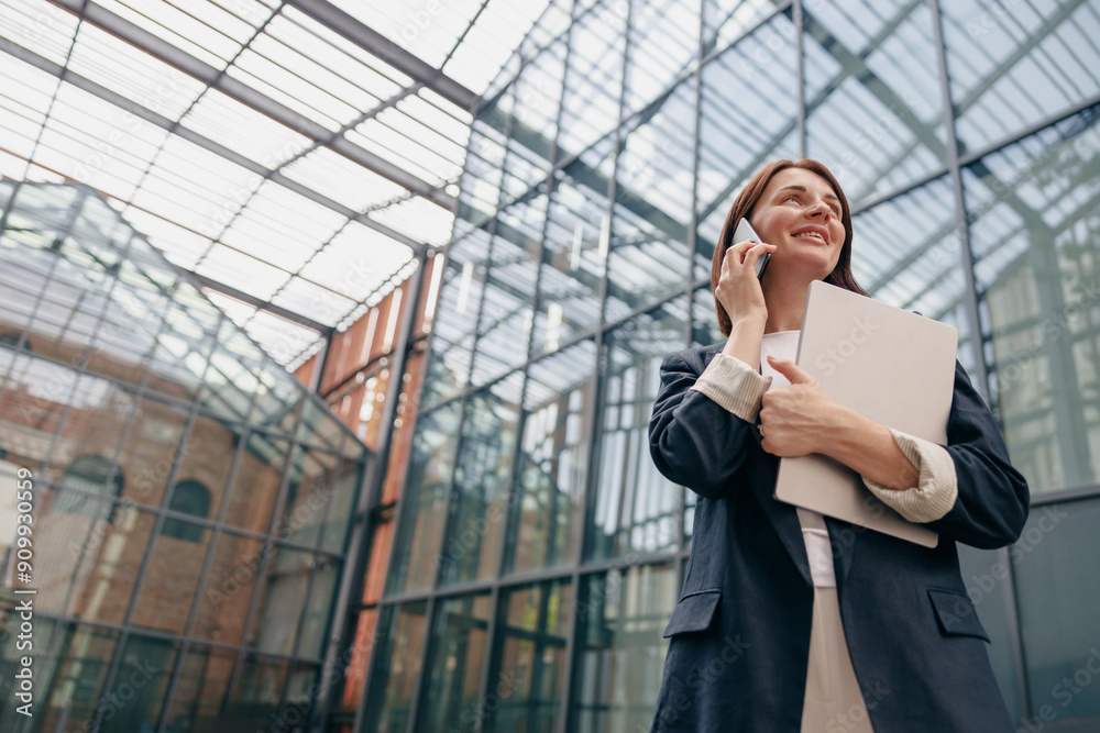 Confident Businesswoman talking on the phone while holding documents in a modern office setting Confident Businesswoman talking on the phone while holding documents in a modern office setting