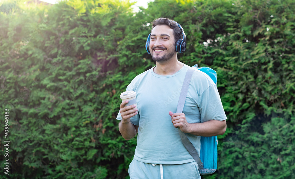 Smiling bearded man in headphones holding takeaway coffee and going to yoga Smiling bearded man in headphones holding takeaway coffee and going to yoga